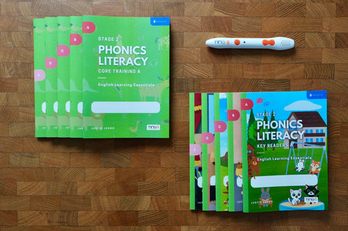 A phonics literacy learning kit arranged on a wooden surface, including green workbook covers, a colorful children's key readers book, and a white tracking pen with orange accents.