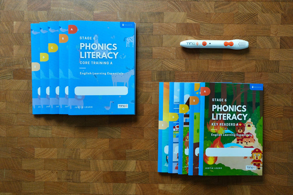 A phonics literacy learning kit arranged on a wooden surface, including light blue workbook covers, a colorful children's key readers book, and a white tracking pen with orange accents.